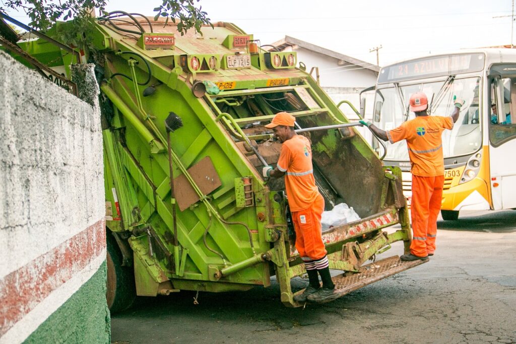 2 funcionários pendurados em um caminhão fazendo coleta de resíduos